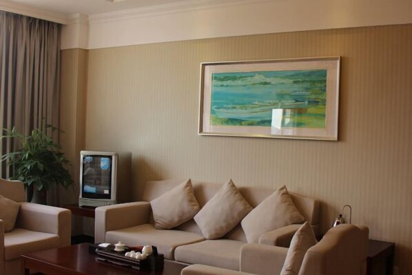 A living room with a beige sofa, a small table with a tray of items, a television, and a framed painting on the wall. - Dabeishan Resort (Jiexi)