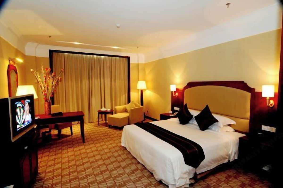 A hotel room with a bed, a TV, a desk, a chair, and a lamp.