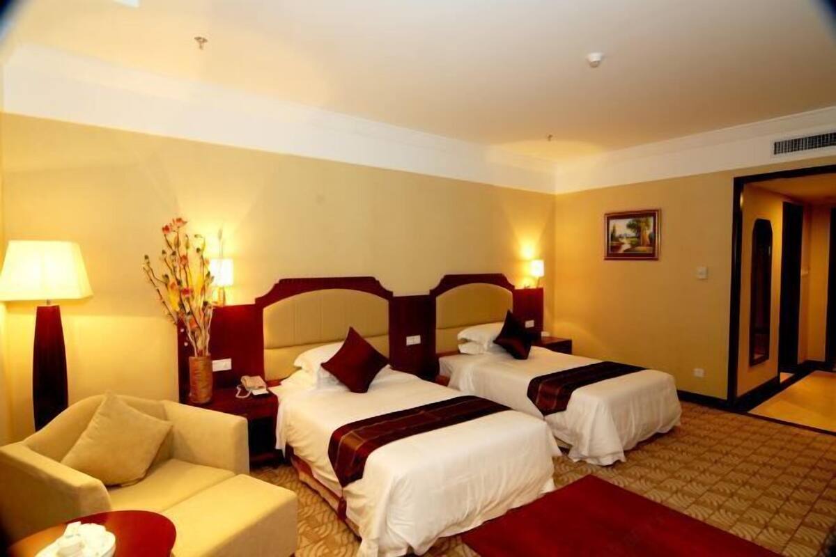 A hotel room with two beds, a sofa, a lamp, and a vase with flowers.