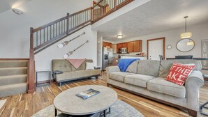 A spacious living area with a staircase, a sofa, a coffee table, and a kitchen in the background.