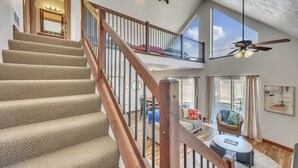 A multi-level home interior with carpeted stairs, a balcony with a ceiling fan, and a dining area with a view.