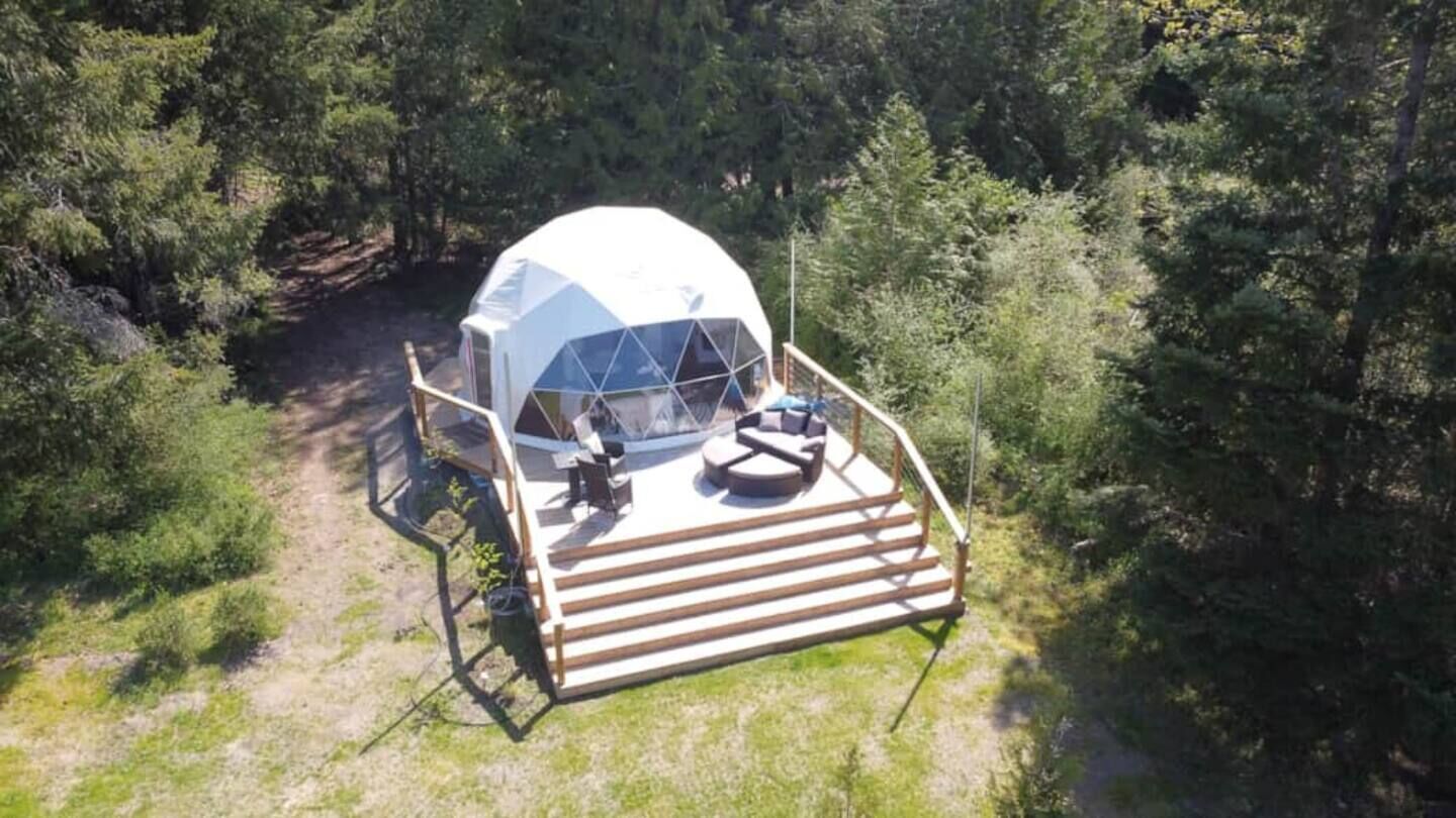 Une structure en forme de dôme géodésique dotée d’une terrasse en bois et d’un espace salon.