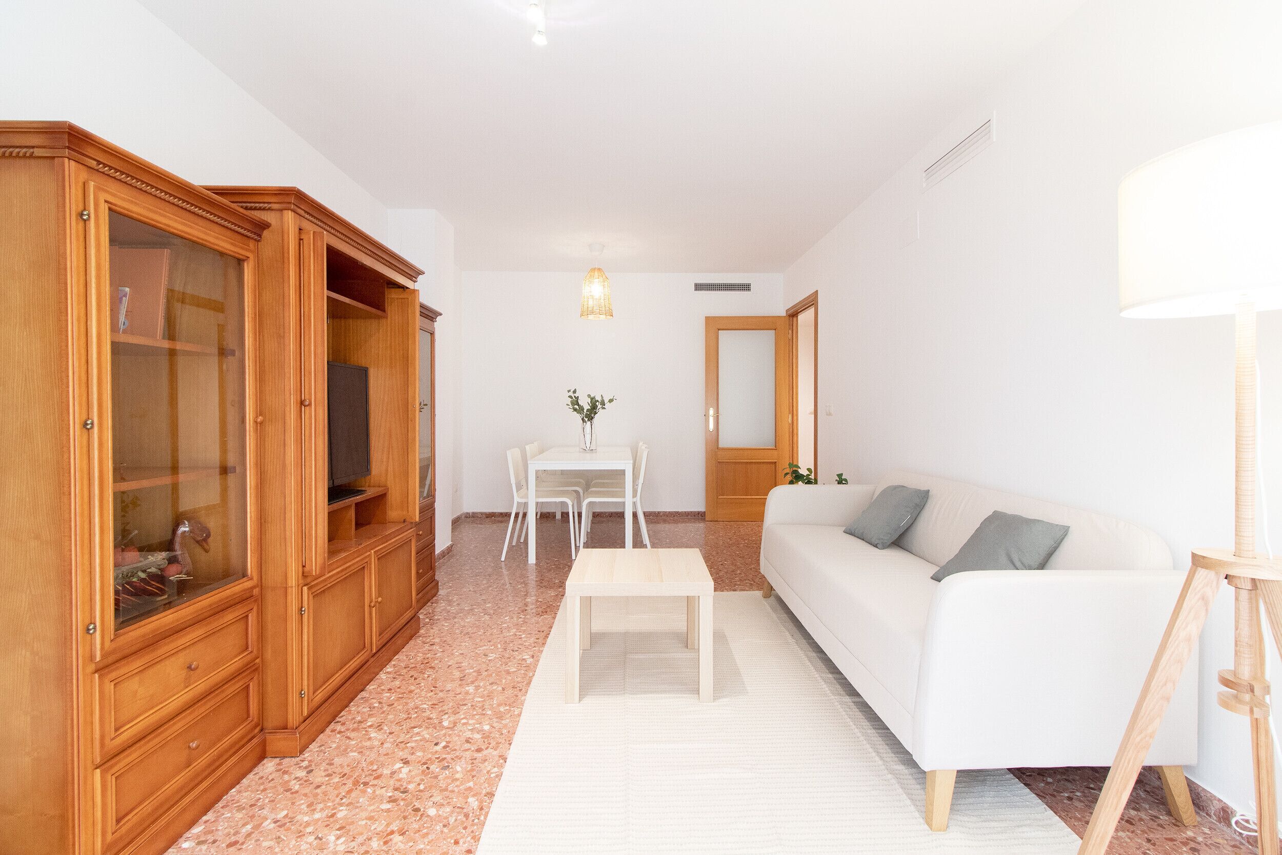 A living room with a white sofa, wooden cabinet, and a small table.