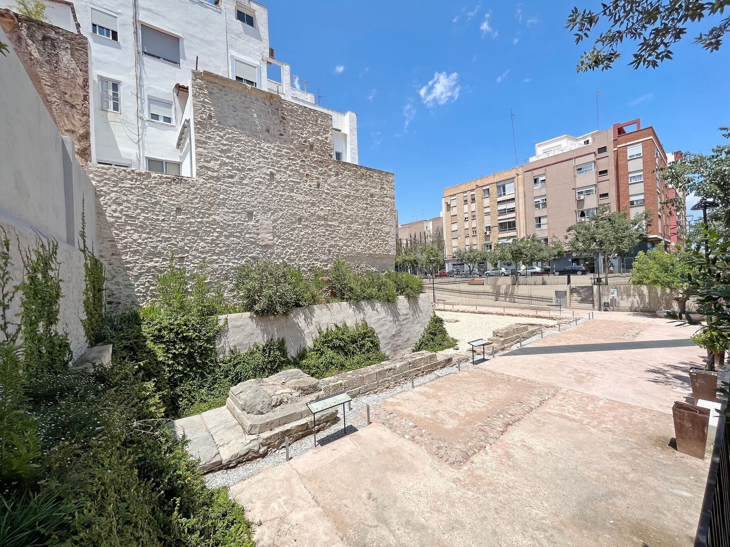 Une cour bordée de murs en pierre, agrémentée de verdure et dotée d’une zone pavée.