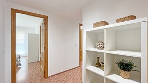 A hallway with a wooden door, a white shelf with decorative items, and a terrazzo floor.