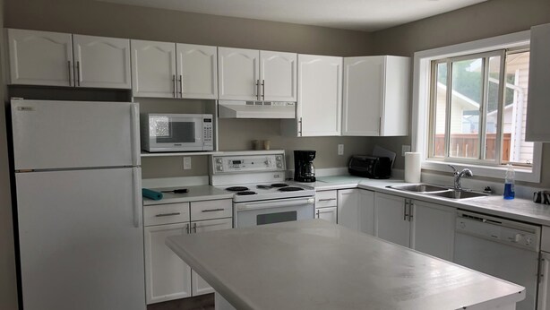 Una cocina moderna con armarios blancos, microondas integrado, estufa, cafetera y lavavajillas.