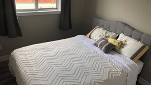 Un dormitorio con cama, cabecera gris y ventana con cortinas.
