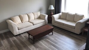 Una sala de estar con dos sofás color beige, una mesa de centro de madera y una lámpara sobre una mesita auxiliar.