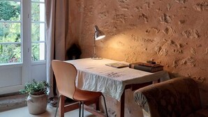 A rustic room with exposed wooden beams, a table with a white tablecloth, a lamp, a chair, a sofa, and a potted plant.
