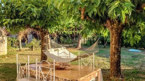 A wooden table with a metal chair and a hammock under a tree.