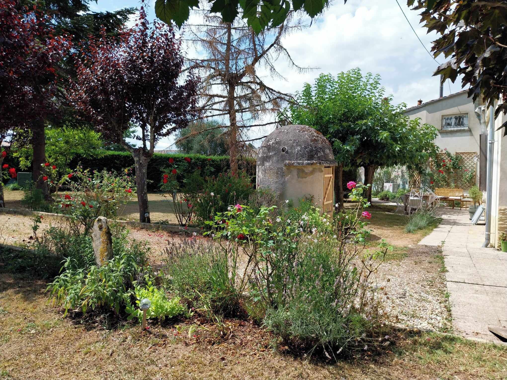 Un jardin avec différentes espèces de plantes et une petite construction en pierre.