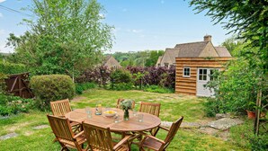 A wooden table with chairs in a garden with a house in the background.