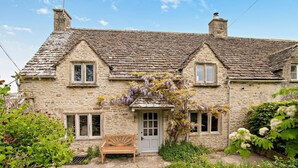 A stone house with a sloped roof, a front door, and a bench in the front yard.