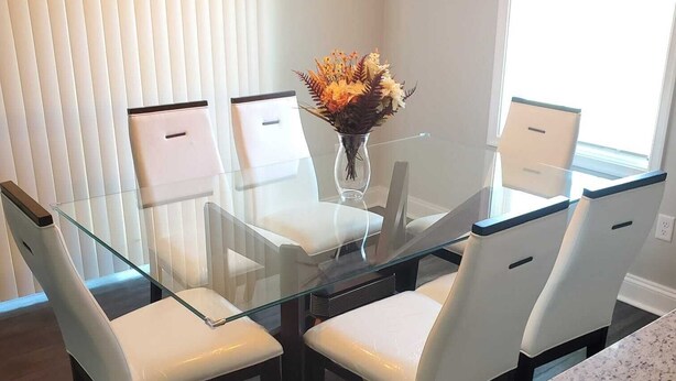 A dining area with a glass table surrounded by white chairs, a vase with flowers, and a chandelier. - Welcome to our newly built house  (Glen Burnie)