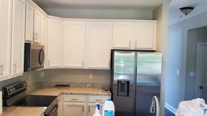 A kitchen with white cabinets, a stainless steel refrigerator, a microwave, and a stove. - Welcome to our newly built house  (Glen Burnie)