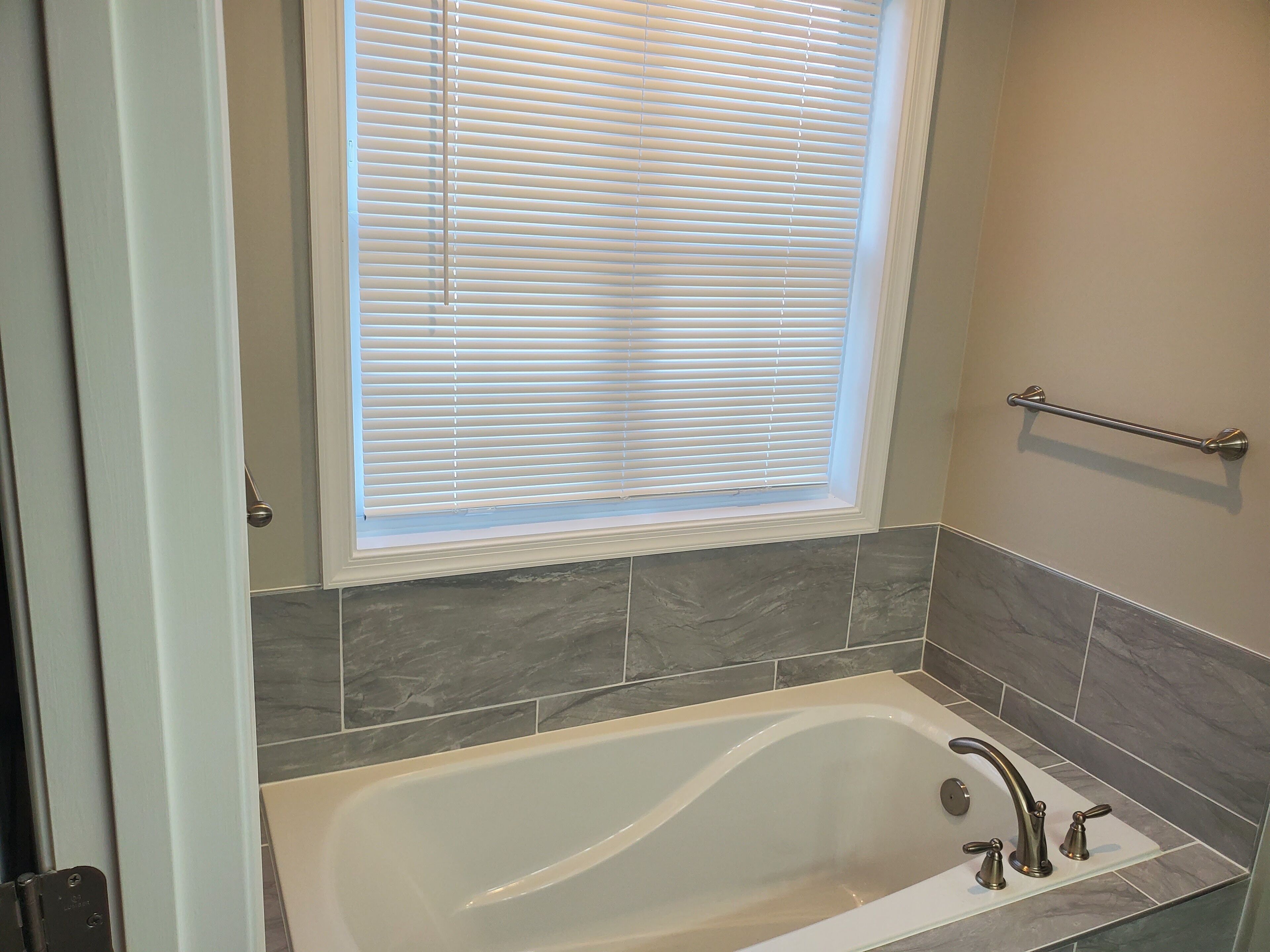 A bathroom with a bathtub, a window with blinds, a towel rack, and tiled walls.