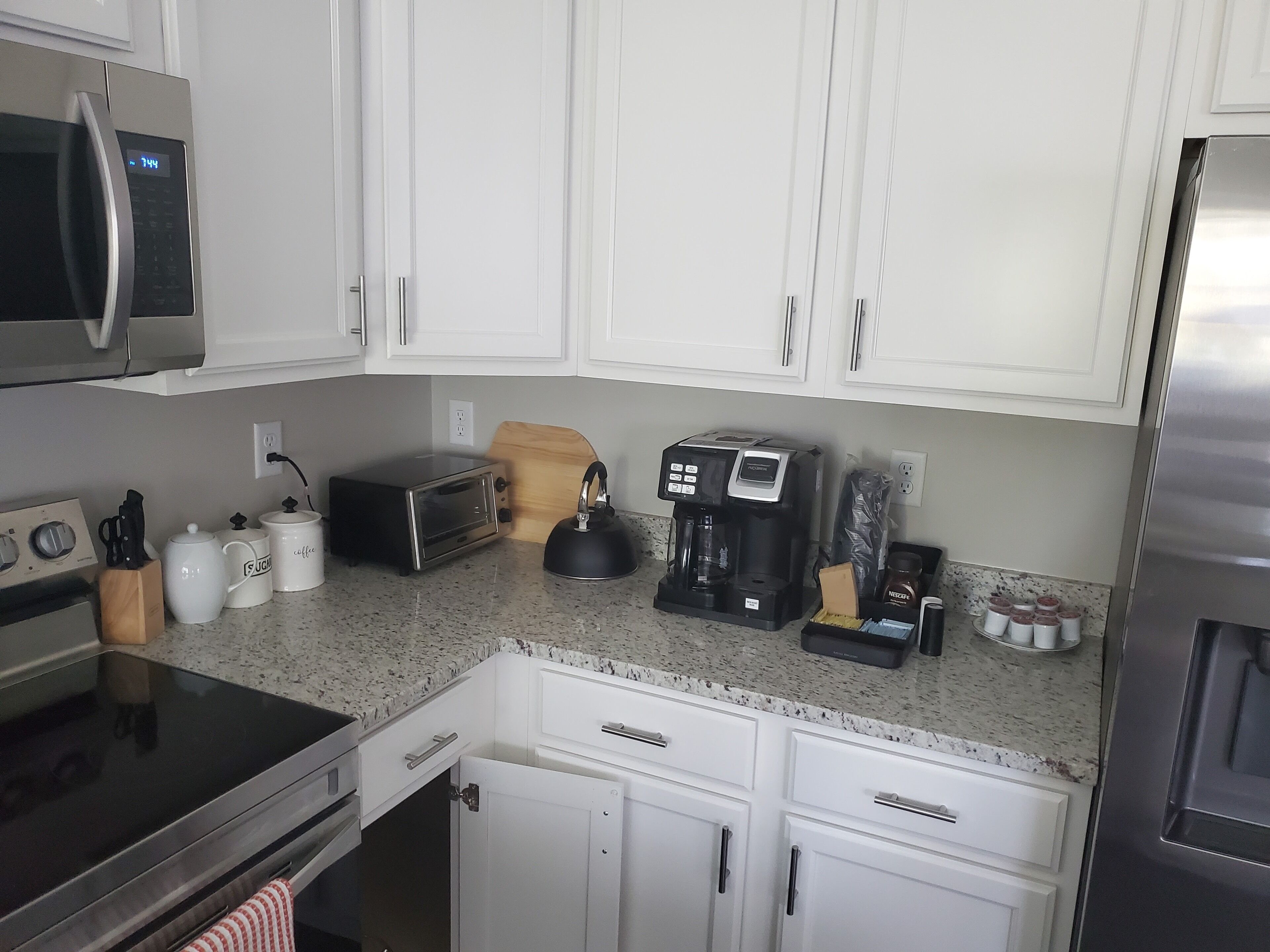 A modern kitchen with white cabinets, a stainless steel refrigerator, a coffee maker, a toaster, and a kettle.