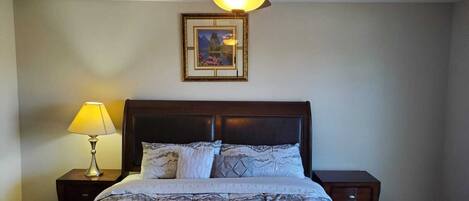 A bedroom with a bed, a nightstand, a lamp, a framed picture on the wall, and a ceiling fan.