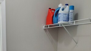 A laundry area with two front-loading washing machines and a shelf with detergent bottles. - Welcome to our newly built house  (Glen Burnie)
