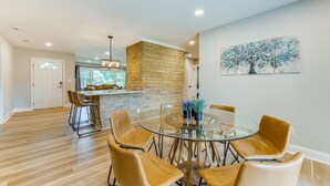 A modern dining area with a glass table surrounded by leather chairs, a stone accent wall, and a view of the kitchen. - Charming Charlotte Home: 2 Mi to Downtown! (Charlotte)