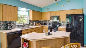Una cocina con armarios de madera, microondas, refrigerador, lavavajillas y pileta.