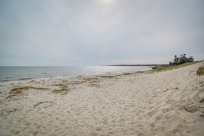 A sandy beach with a house on a hill overlooking the sea. - Walk to Beach: Chatham Gem w/ Ocean-View Sunroom! (Chatham)