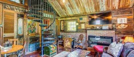 A rustic interior with a wooden ceiling, a fireplace, a television, and a dining area with a table and chairs.