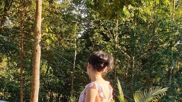 Una persona seduta sul bordo di una piscina, circondata da vegetazione rigogliosa.