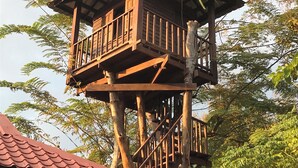 Una casetta sugli alberi di legno con diversi piani e un balcone, immersa nel verde.