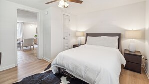 Een slaapkamer met een bed, nachtkastjes, een plafondventilator en een deur naar een andere kamer.