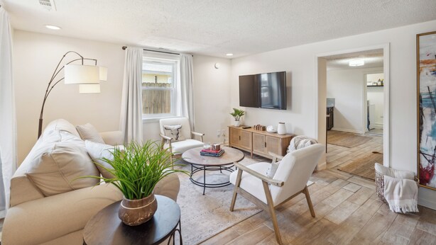 Een moderne woonkamer met een bank, fauteuils, een salontafel en een aan de muur bevestigde televisie.