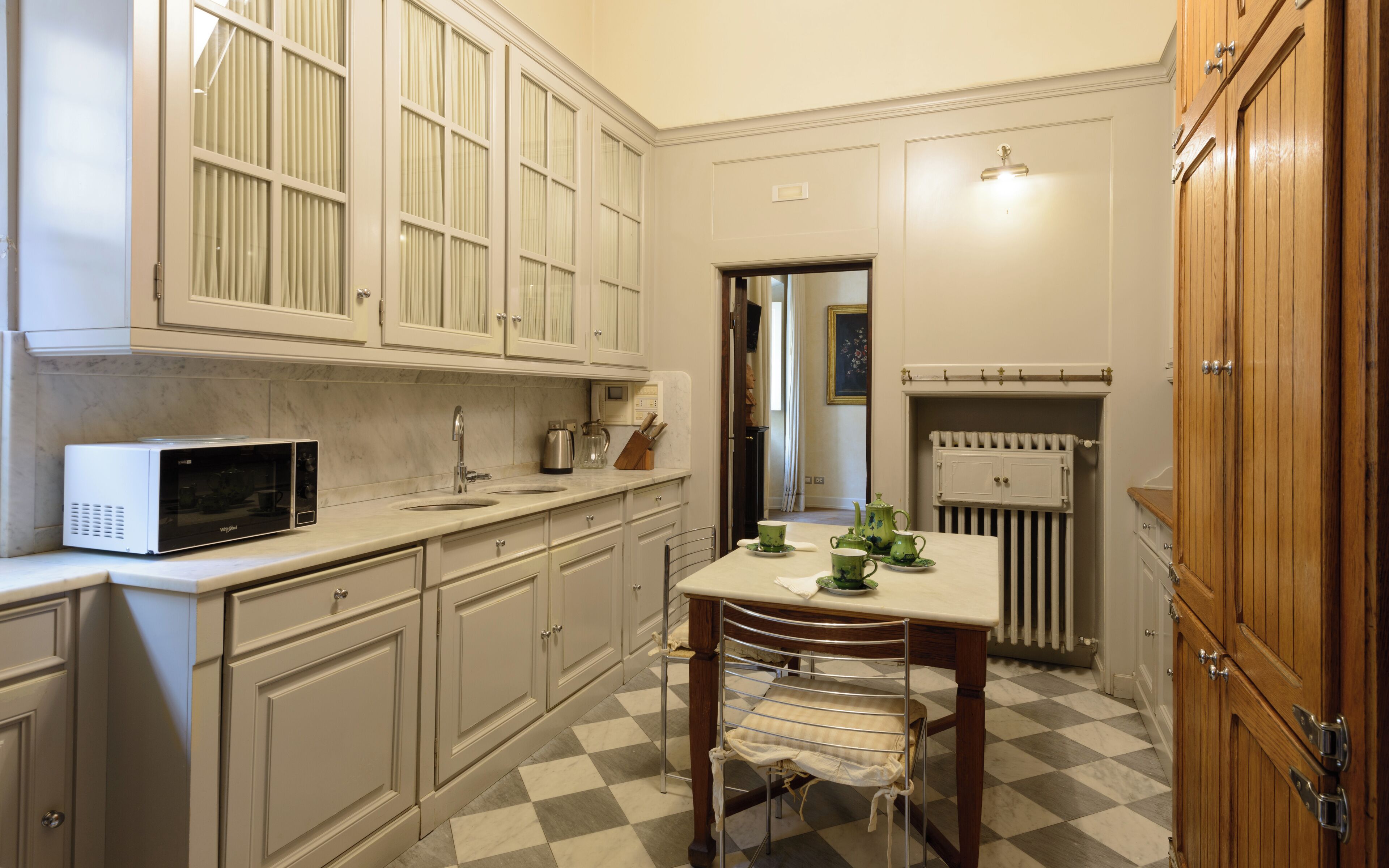 A kitchen with white cabinets, a microwave, a sink, and a radiator.
