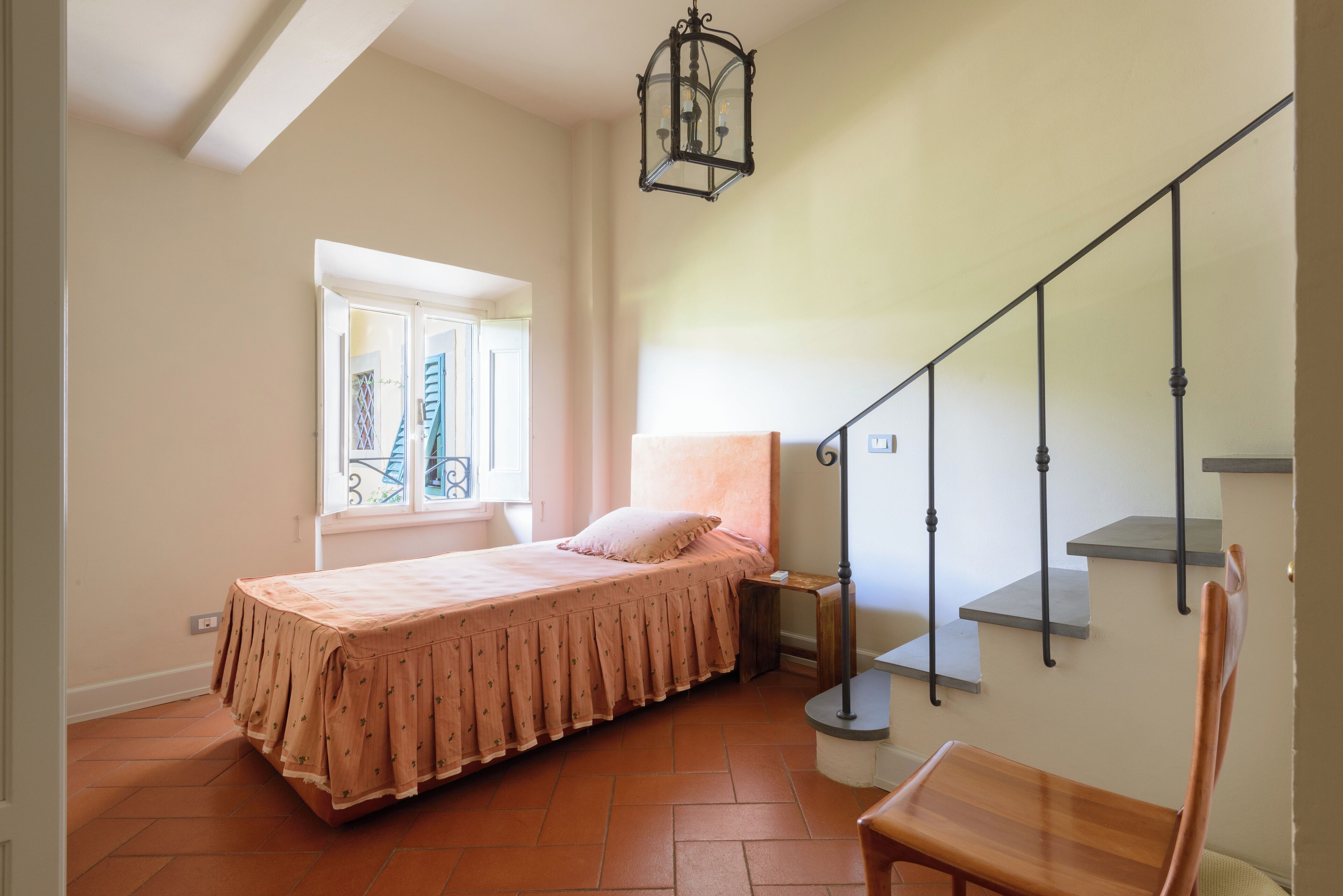 A bedroom with a bed, a window, a staircase, and a chair.