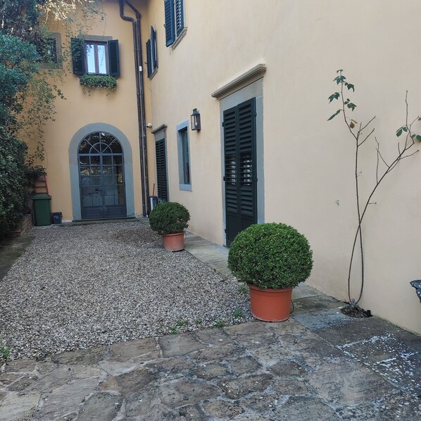 Un patio con suelo de piedra, una planta en maceta redonda y un edificio con puerta y ventanas.