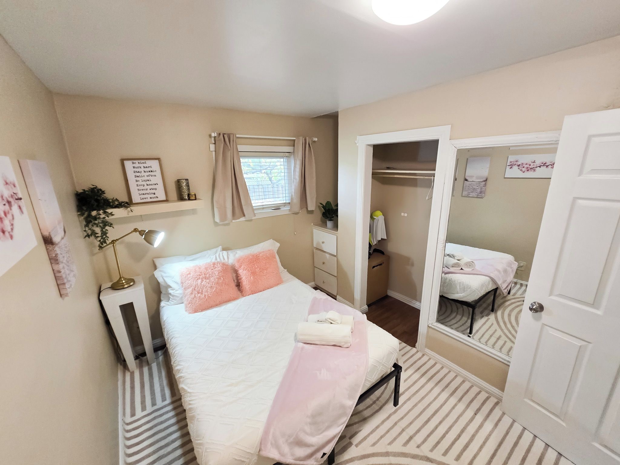 Un dormitorio con cama, lámpara de noche, espejo y ventana con cortinas.