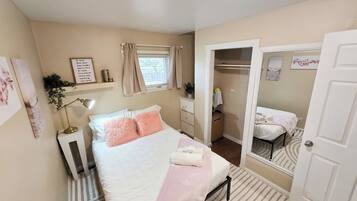 Un dormitorio con cama, lámpara de noche, espejo y ventana con cortinas.