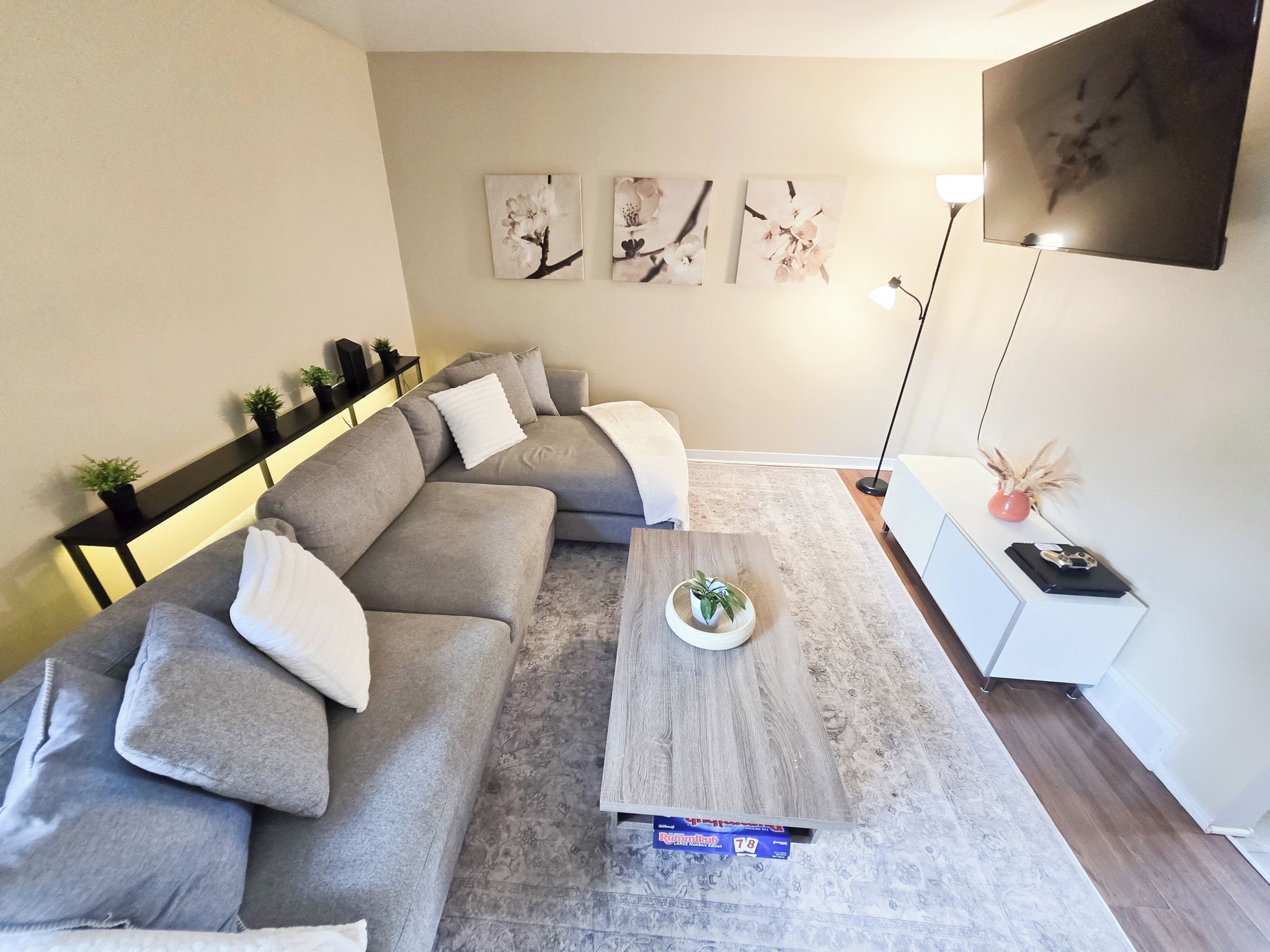 Un salon moderne avec un canapé d’angle gris, une table basse et une table d’appoint blanche.