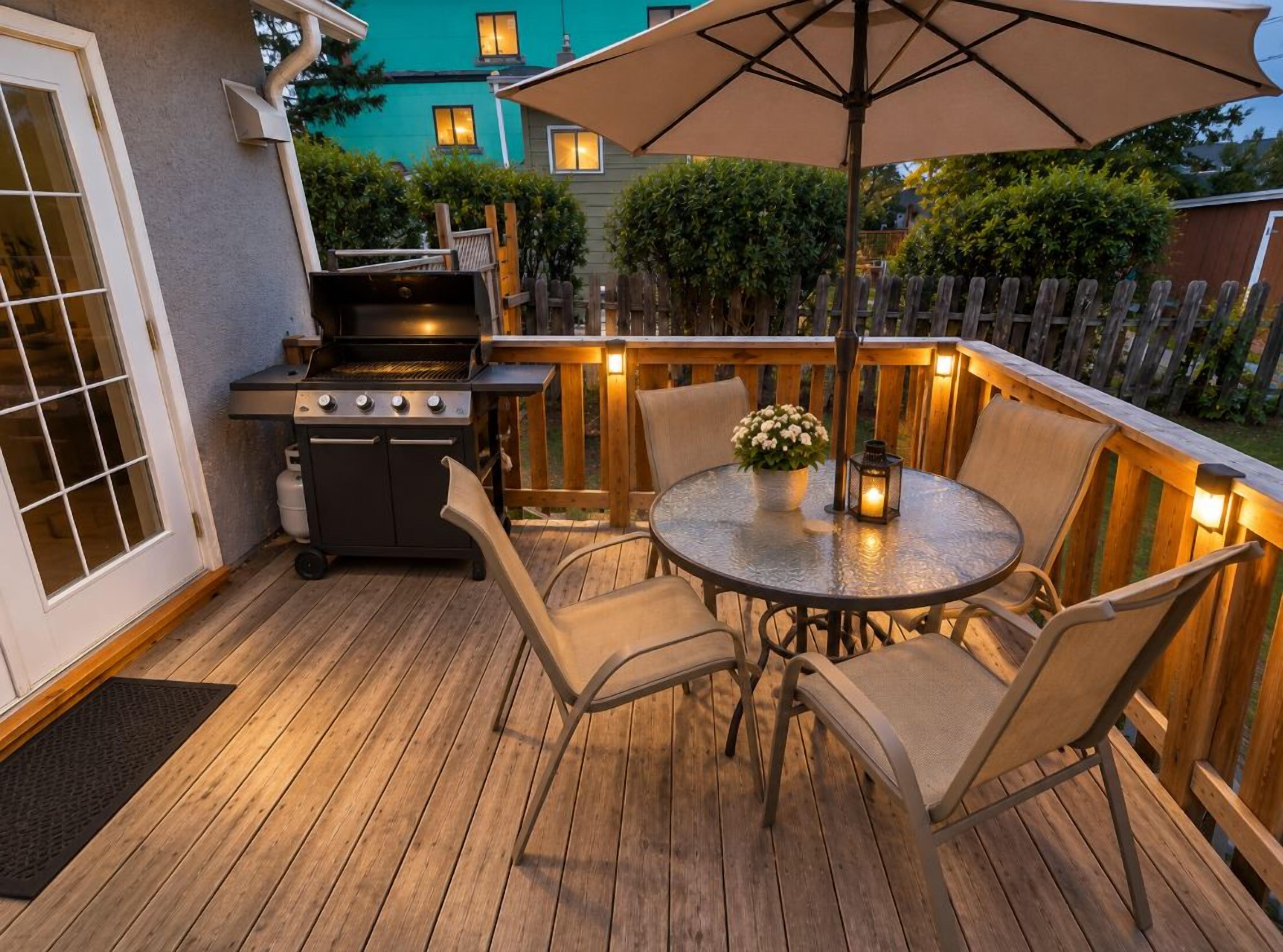 An outdoor patio with a grill, round table, chairs, and a large umbrella.
