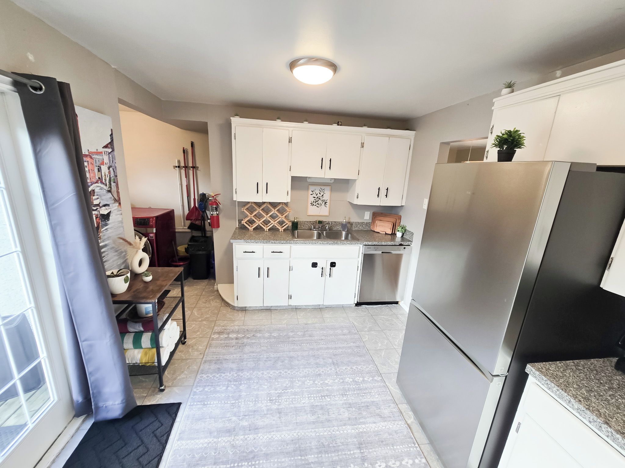 Una cocina compacta con armarios blancos, un refrigerador de acero inoxidable y un salpicadero de azulejos.