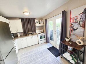 A kitchen with white cabinets, a stove, and a window with curtains. - Family House with Httb Playgr BBQ Firept (Calgary)