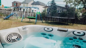 A hot tub with a view of a backyard with a swing set and a trampoline. - Family House with Httb Playgr BBQ Firept (Calgary)