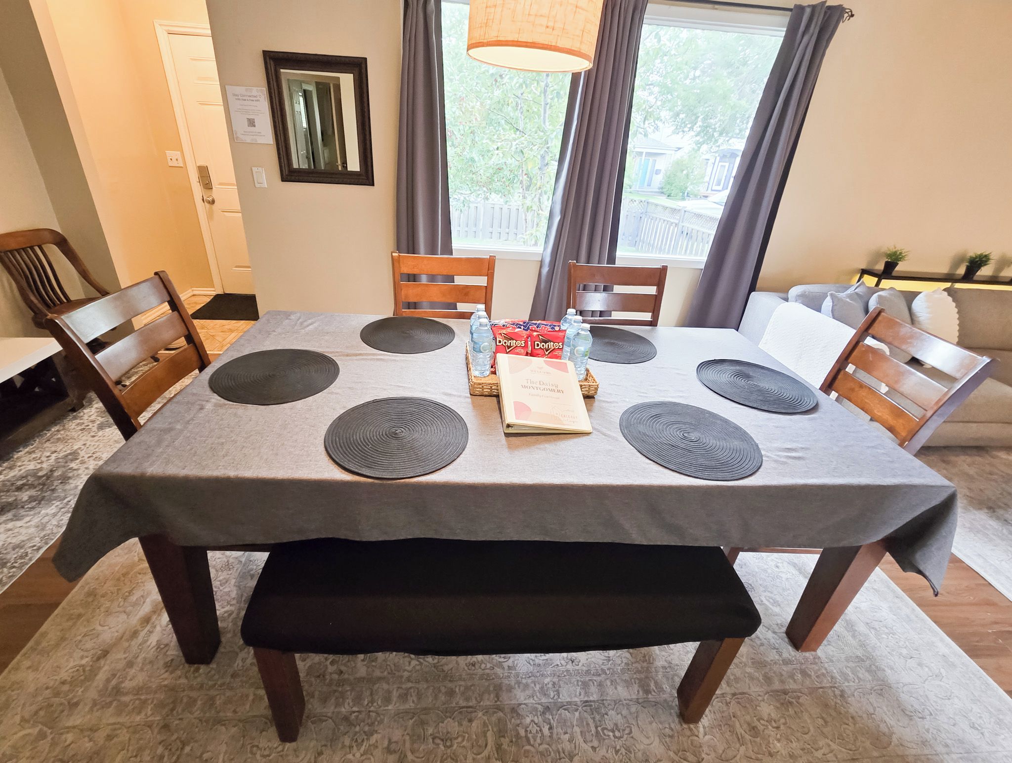 A dining table with a grey tablecloth, six black placemats, and a center tray with snacks and a book.