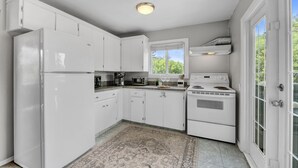 A kitchen with white cabinets, a refrigerator, a stove, and a window with a view of greenery. - Family House with Httb Playgr BBQ Firept (Calgary)