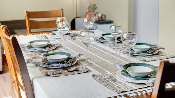 A dining table set with plates, bowls, and wine glasses, arranged on a striped table runner. - Family House with Httb Playgr BBQ Firept (Calgary)