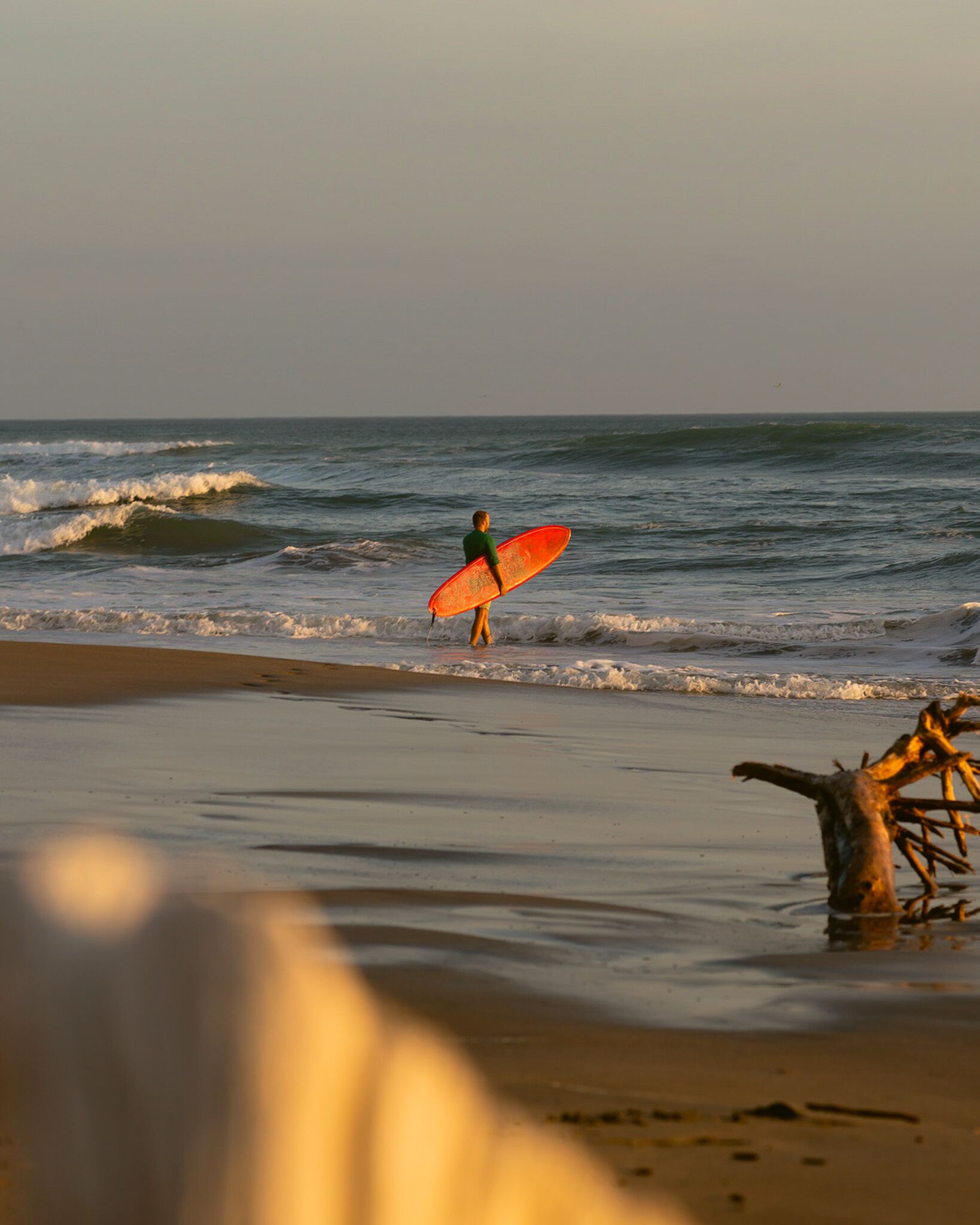 A beach scene with a surfer walking towards the ocean carrying a surfboard.
