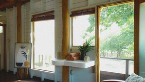 Quarto com piso de madeira, piaça branca, janela com vista para árvores e quadro na parede.