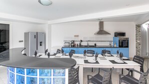 A modern kitchen with a central island, a dining area with a curved table, and a view of the living area.