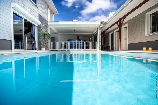 Ein Schwimmbecken mit überdachter Terrasse, einer Steinsäule und Blick auf den Himmel.