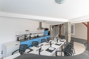 Eine kompakte Küche mit blauen Schränken, einem weißen Kühlschrank und einem Essbereich mit einem langen Tisch, gedeckt für vier Personen.
