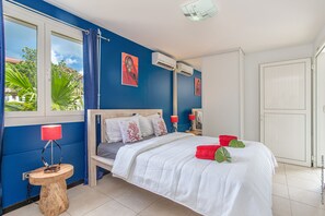 Ein Schlafzimmer mit Bett, Nachttisch, Lampe und einem Fenster mit Vorhängen.